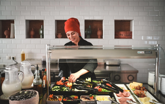 Köchin steht hinter einer Vitrine und präsentiert leckeres Essen