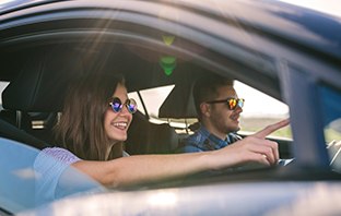 Pärchen sitzt im Auto und freut sich auf den Urlaub mit Eigenanreise