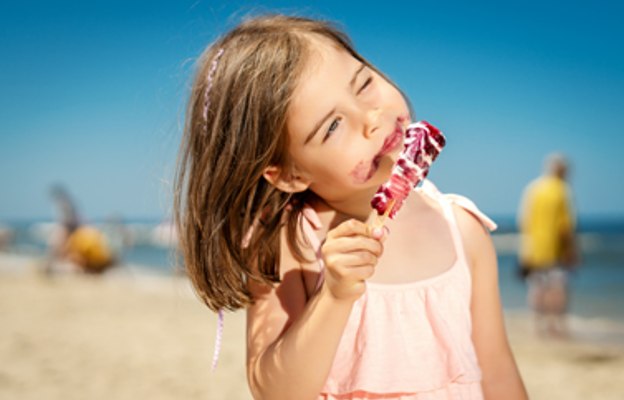 Kleines Mädchen mit buntem Eis am Strand