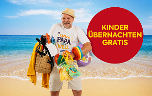 Thomas Stipsits steht am Strand und trägt viele Strandutensilien