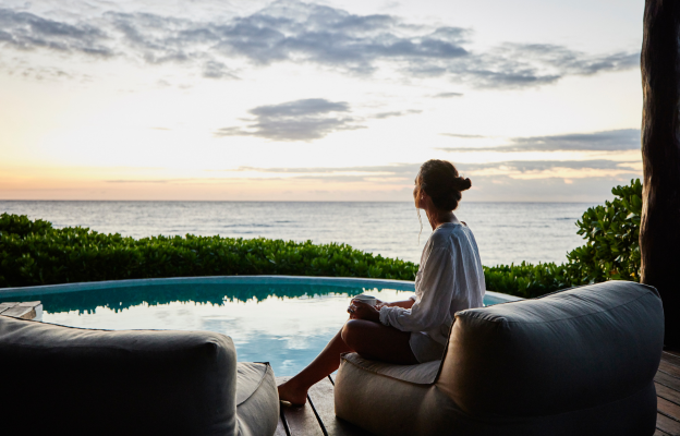 Frau sitzt auf einer Designer Liege am Pool mit Aussicht auf das Meer in einem Luxushotel
