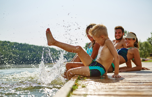Familie sitzt an einem Steg und plantscht mit den Füßen im See