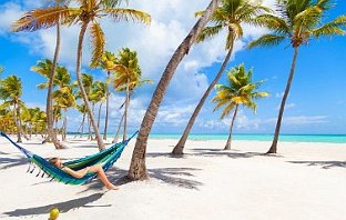 Eine Frau liegt in einer Hängematte, die in paradiesischen Umgebung aufgehangen ist