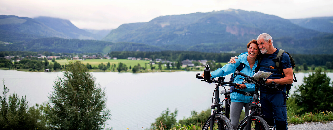 Radfahrerin auf der Weide mit See und Bergen im Hintergrund