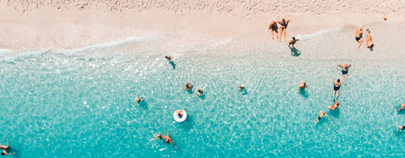 Schöner Strand mit hellblauem Wasser und vielen Personen beim Baden