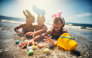 Kinder mit Osterhasen Ohren spielen am Strand 