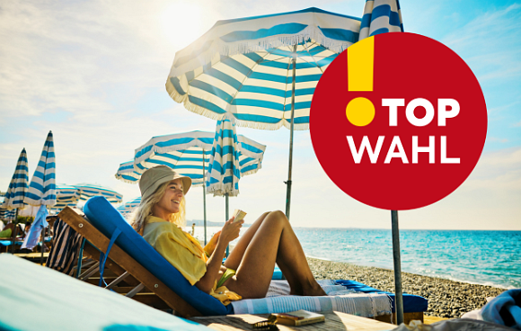 Thomas Stipsits steht am Strand mit vielen Badeutensilien 