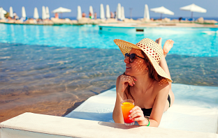 Frau liegt am Pool mit einem Getränk